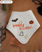 Load image into Gallery viewer, A white bandana with 'Spooky Season' text and embroidered bats, ghosts, and pumpkins on a merle gray yarn. It features a snap-on style for pets.