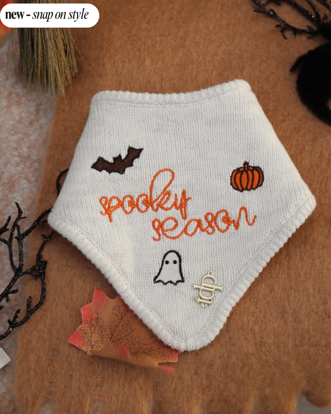 A white bandana with 'Spooky Season' text and embroidered bats, ghosts, and pumpkins on a merle gray yarn. It features a snap-on style for pets.